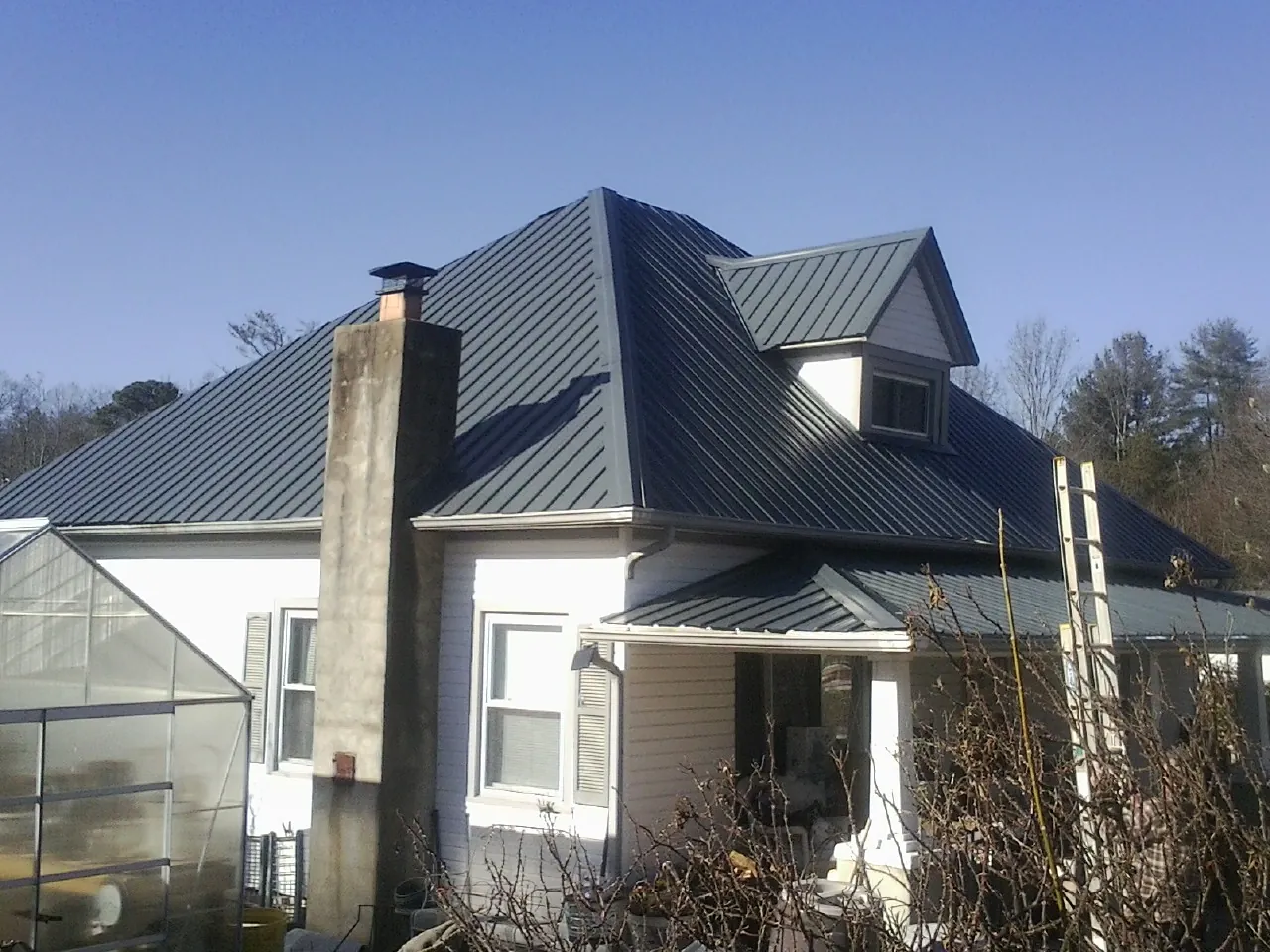 Dark blue standing seam metal roof on a white farmhouse with dormer — Slate & Tile Roof Repair by Roofing Brothers in Searchlight