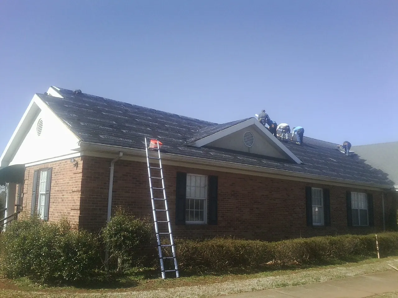Crew tearing shingles off a brick ranch roof with a ladder set — Metal Roof Repair work by our crew in Searchlight