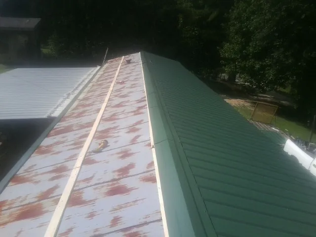Old rusted panels beside newly installed green metal roofing — Wind Damage Roof Repair by Roofing Brothers in Searchlight