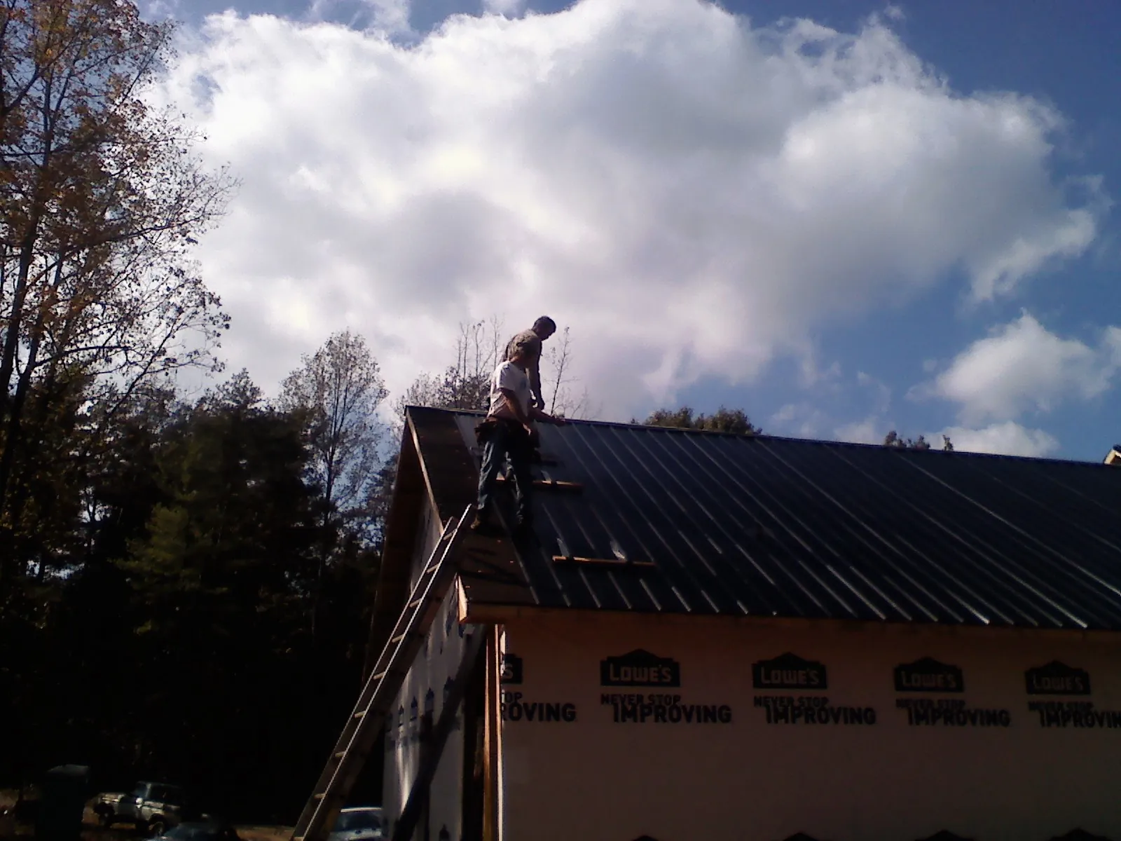 Roofer fastening dark metal panels high against a cloudy sky, from a Roof Inspection job in Searchlight